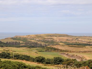 A rural landscape with grassy fields shrubs and hills with a body of water in the background at Shepherd's Stone in Llanfairynghornwy near Llanfaethlu