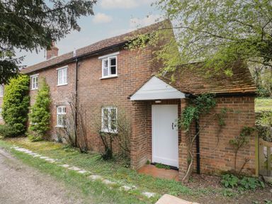 A brick cottage with white door and windows surrounded by greenery at Chalkpit Cottage in Blewbury