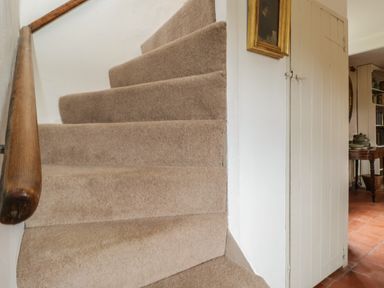 A carpeted staircase with a wooden handrail next to a white door leading to a room with a table at Chalkpit Cottage in Blewbury