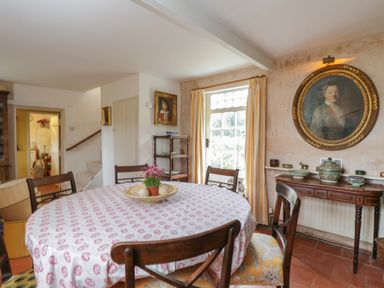A dining room with a round table covered by a patterned tablecloth and wooden chairs at Chalkpit Cottage in Blewbury