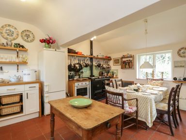 A kitchen with a wooden table and dining area with chairs a refrigerator and hanging pots at Chalkpit Cottage in Blewbury