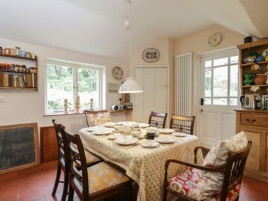 A dining room with a set table and wooden chairs near a window and a door at Chalkpit Cottage in Blewbury