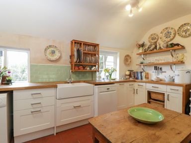 A kitchen with white cabinets wood countertops a farmhouse sink and decorative plates on the walls at Chalkpit Cottage in Blewbury
