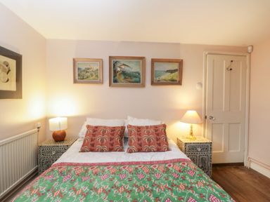 A bedroom with a bed between two patterned bedside tables with lamps and three paintings above the bed at Chalkpit Cottage in Blewbury