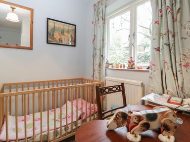 A nursery room with a wooden crib a table with a toy dog and a floral curtain at Chalkpit Cottage in Blewbury