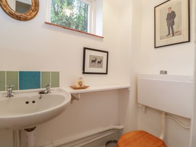 A small bathroom with a sink a shelf with soap a window and framed pictures at Chalkpit Cottage in Blewbury