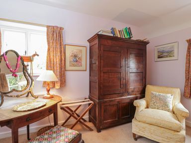 A room with a wooden wardrobe armchair a dressing table with a mirror and a lamp at Chalkpit Cottage in Blewbury