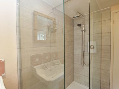 A shower area with glass partition a wall-mounted showerhead and a sink reflected in the glass at Chalkpit Cottage in Blewbury