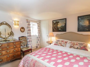 A bedroom with a double bed a wooden dresser a chair and two paintings on the wall at Chalkpit Cottage in Blewbury