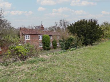 A brick house with white windows surrounded by trees and grass at Chalkpit Cottage in Blewbury