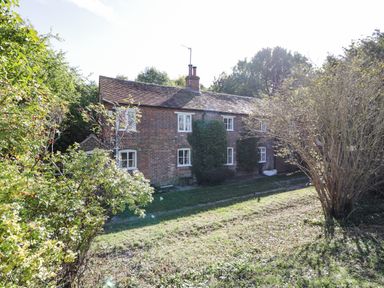 A brick house with a tiled roof surrounded by trees and bushes at Chalkpit Cottage in Blewbury