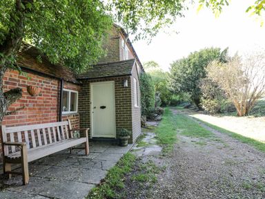 A brick house entrance with a wooden bench and a gravel path beside it at Chalkpit Cottage in Blewbury