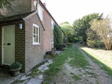 A brick house with white framed windows along a grassy dirt path with trees and bushes at Chalkpit Cottage in Blewbury