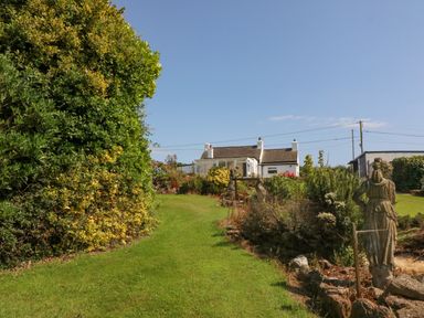 A garden with a grass path leading to a white house with a conservatory and statues in the garden at Pen Bonc in Llanddaniel Near Gaerwen