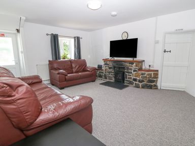 A living room with two brown leather sofas a flat screen tv on a stone fireplace and a window with curtains at Pen Bonc  Llanddaniel Near Gaerwen