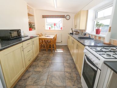 A kitchen with wooden cabinets a dining table with chairs a stove microwave and windows at Pen Bonc in Llanddaniel Near Gaerwen