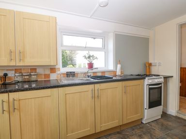 A kitchen with wooden cabinets a black countertop a sink with drying rack a window a stove and kitchen utensils at Pen Bonc in Llanddaniel Near Gaerwen