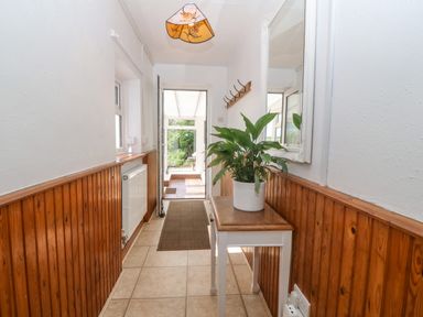 A hallway with tiled floor wood paneling a small table with a plant a wall mirror coat hooks and a door leading outside at Pen Bonc in Llanddaniel Near Gaerwen