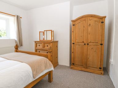 A bedroom with a wooden bed chest of drawers with a mirror and a wardrobe at Pen Bonc Llanddaniel Near Gaerwen