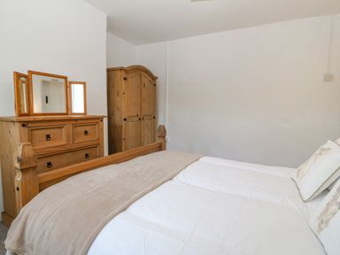 A bedroom with a wooden bed, wooden dresser with mirror, and wooden wardrobe at Pen Bonc in Llanddaniel Near Gaerwen