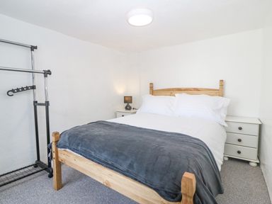 A bedroom with a wooden bed white bedding gray blanket two white bedside cabinets and a clothes rack at Pen Bonc in Llanddaniel Near Gaerwen