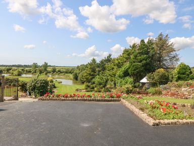 A garden with flower beds and trees overlooking a pond and fields at Pen Bonc in Llanddaniel Near Gaerwen