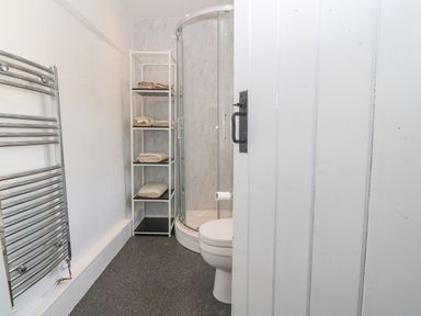 A bathroom with a corner shower unit toilet towel rack and shelving with towels at Pen Bonc Llanddaniel Near Gaerwen