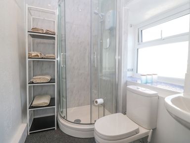 A bathroom with a corner shower cubicle toilet shelf with towels and a window at Pen Bonc Llanddaniel Near Gaerwen