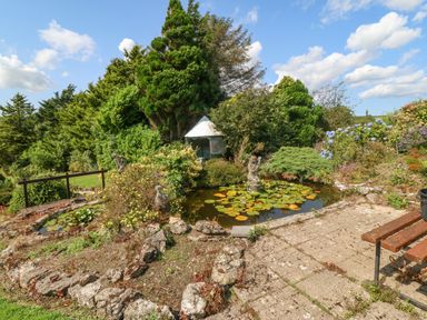 A garden with a small pond filled with lily pads statues a bench stone pathway and trees at Pen Bonc  in Llanddaniel Near Gaerwen