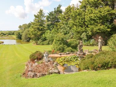 A garden with a small pond covered in lily pads surrounded by statues and trees at Pen Bonc in Llanddaniel Near Gaerwen