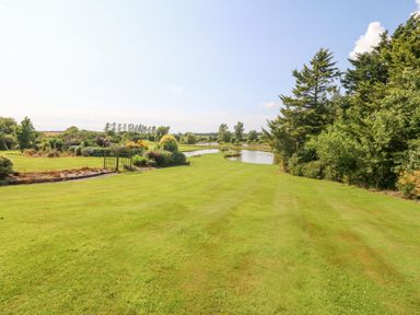 A large grassy garden with trees and a pond at Pen Bonc in Llanddaniel Near Gaerwen