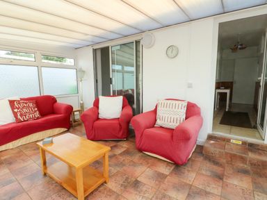 A conservatory with red sofas and a coffee table at Pen Bonc in Llanddaniel Near Gaerwen