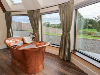 A bathroom with a copper bathtub beside large windows at Ty Crwn in Lampeter