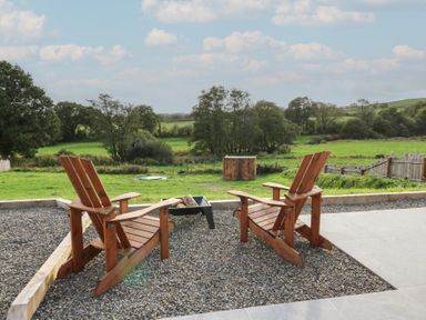 A seating area with chairs and a fire pit overlooking a field at Ty Crwn in Lampeter
