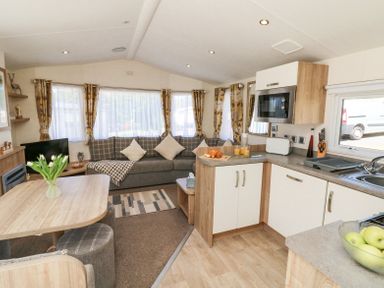 An open plan living area with a kitchen and dining table with flowers and a living room with a sofa and TV at Horizon in Combe Martin