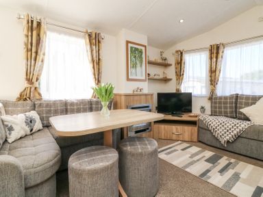 A living room with two grey sofas a wooden table and two stools a television on a wooden stand and curtains at Horizon in Combe Martin