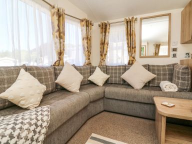 A corner sofa with cushions and a rolled towel in a living room with floral curtains and a wall mirror at Horizon in Combe Martin