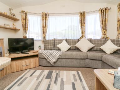 A living room with a grey sectional sofa and patterned cushions with a television on a wooden stand at Horizon in Combe Martin
