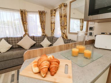 A kitchen counter with croissants and juice in glasses next to a sofa with cushions and floral curtains at Horizon in Combe Martin