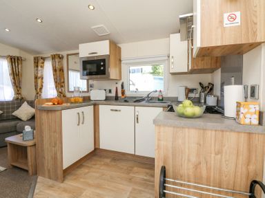 A kitchen with countertop microwave toaster and fruit bowl next to a living area with sofa and curtains at Horizon in Combe Martin