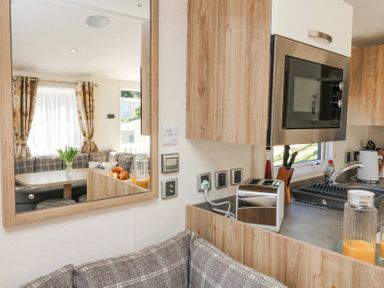 A kitchen with a toaster microwave sink and utensils reflected in a mirror showing a dining area with a table sofa croissants and flowers at Horizon in Combe Martin
