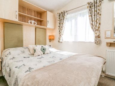 A bedroom with a bed cushions curtains and overhead cabinets at Horizon in Combe Martin