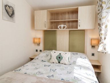 A bedroom with a bed with butterfly bedspread two wall-mounted lights above small shelves and a cabinet on the wall at Horizon in Combe Martin
