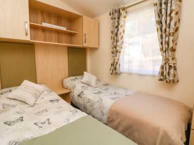 A bedroom with two single beds with butterfly bedspreads a window with patterned curtains and overhead wooden cabinets at Horizon in Combe Martin