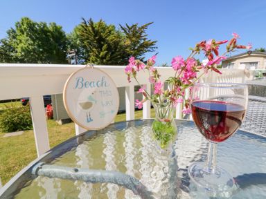 A glass table on a balcony with a vase of pink flowers a glass of red wine and a sign reading Beach This Way at Horizon Combe Martin