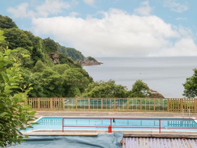 An outdoor swimming pool with safety rails overlooking a wooded hillside and the sea at Horizon in Combe Martin
