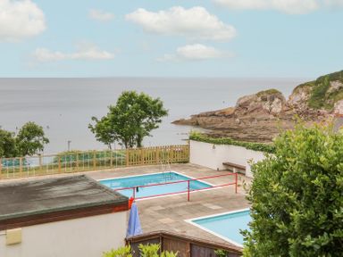 An outdoor swimming pool area overlooking the sea with trees rocks and bushes at Horizon in Combe Martin