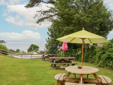 Picnic tables with umbrellas on grass overlooking sea with trees in background at Horizon in Combe Martin