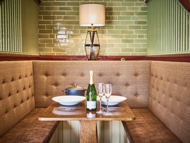A dining nook with a wooden table set with plates glasses a bottle and a pot at The Stallion in Humshaugh