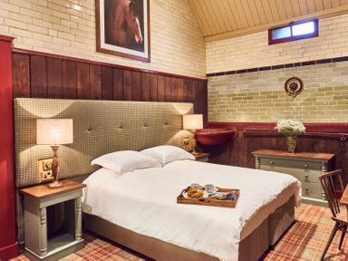 A bedroom with a double bed a tray with coffee and croissants two bedside tables with lamps a chest of drawers with flowers and a framed horse picture on the wall at The Stallion in Humshaugh